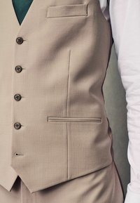 Gilet beige avec cinq boutons, poche latérale et design élégant. Le matériau a une texture lisse avec un léger éclat.