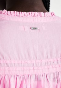 Camicia in cotone rosa con colletto arricciato, caratterizzata da cuciture orizzontali, un'etichetta sottile argentata e una consistenza morbida.