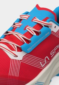 Ερυθρό και κυανό αθλητικό παπούτσι με κορδόνια λευκής ραβδωτής σχεδίασης, ραμμένες λεπτομέρειες και λευκή σόλα, με το λογότυπο La Sportiva στην πλευρά.