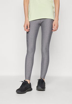 Leggings grigi con taglio aderente e finitura testurizzata, caratterizzati da un logo nero di lato. Abbinati a scarpe da ginnastica nere per un look sportivo.
