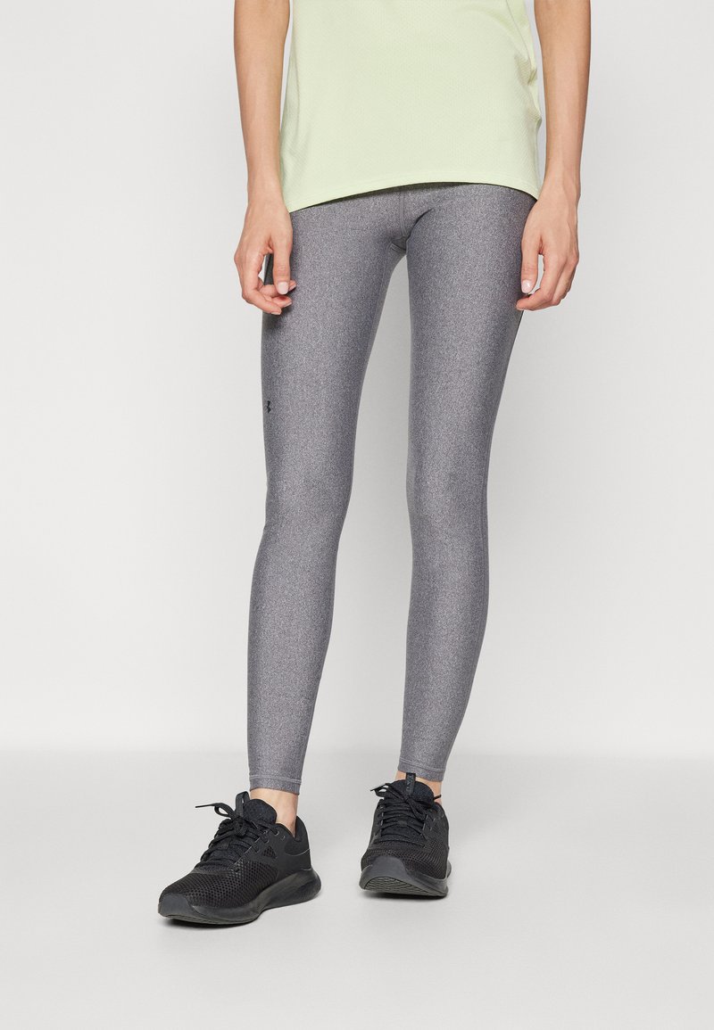 Leggings grigi con taglio aderente e finitura testurizzata, caratterizzati da un logo nero di lato. Abbinati a scarpe da ginnastica nere per un look sportivo.
