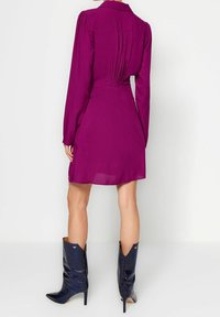 Fuchsiaröd långärmad klänning med en figurnära midja och veckad baksida, i kombination med strukturerade knäförslutande stövlar i mörkblått med spetsiga tår.