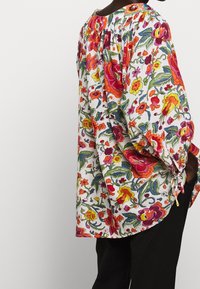 Květinová blůza s živými červenými, růžovými a žlutými vzory na bílém pozadí, s volným střihem a nařaseným výstřihem.