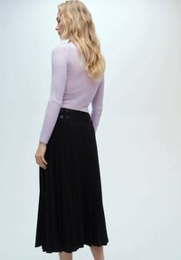 Lichtpaarse geribbelde lange mouw trui gecombineerd met een zwarte geplooide midi rok, met een soepele textuur en strakke taillebanddetails.