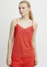Camiseta roja de tirantes hecha de una tela suave, con un borde de encaje en el escote y tirantes finos ajustables. Complementada con pantalones rojos a juego.