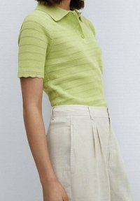 Světlé zelené polo tričko s krátkým rukávem, se zvlněným lemem, texturovaným pletením a třemi knoflíky, doplněné o světle béžové kalhoty.