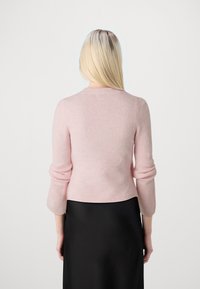 Maglione di lana rosa chiaro con maniche a tre quarti, scollo rotondo, orlo a coste, texture morbida, esposto su uno sfondo neutro.