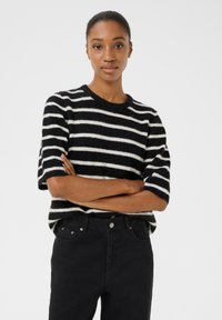 Černobílý pruhovaný svetr s krátkým ruk�ávem v měkké, nadýchané textuře, kombinovaný s černými džíny s vysokým pasem, které mají standardní kovové prvky.