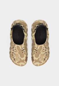 Ζεύγος μπεζ και καφέ Crocs με μοτίβο καμουφλάζ, μαύρες εσωτερικές σόλες και ρυθμιζόμενους ιμάντες στο πίσω μέρος, σε θέα από πάνω.