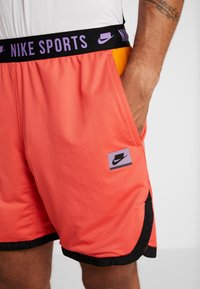 Shorts de sport Nike en coral vif avec une texture en mesh, dotés d'une taille élastique noire et de poches latérales. Comprend un patch logo.