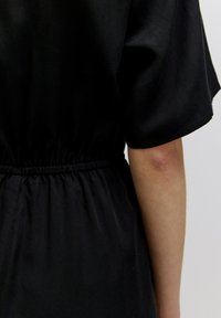 Zwarte jurk met korte mouwen, verzamelde taille en een gladde textuur, met een ontspannen pasvorm en minimalistisch ontwerp.