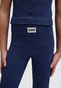 Marinblå ribbad träningsset som består av en åtsittande topp och tights med en logotyp på midjebandet. Slät tyg med lätt stretch.