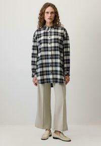 Crno-bijela karirana košulja s dugim rukavima, uparena s bež širokim hlačama i svijetlim mokasinkama. Jednostavan dizajn.