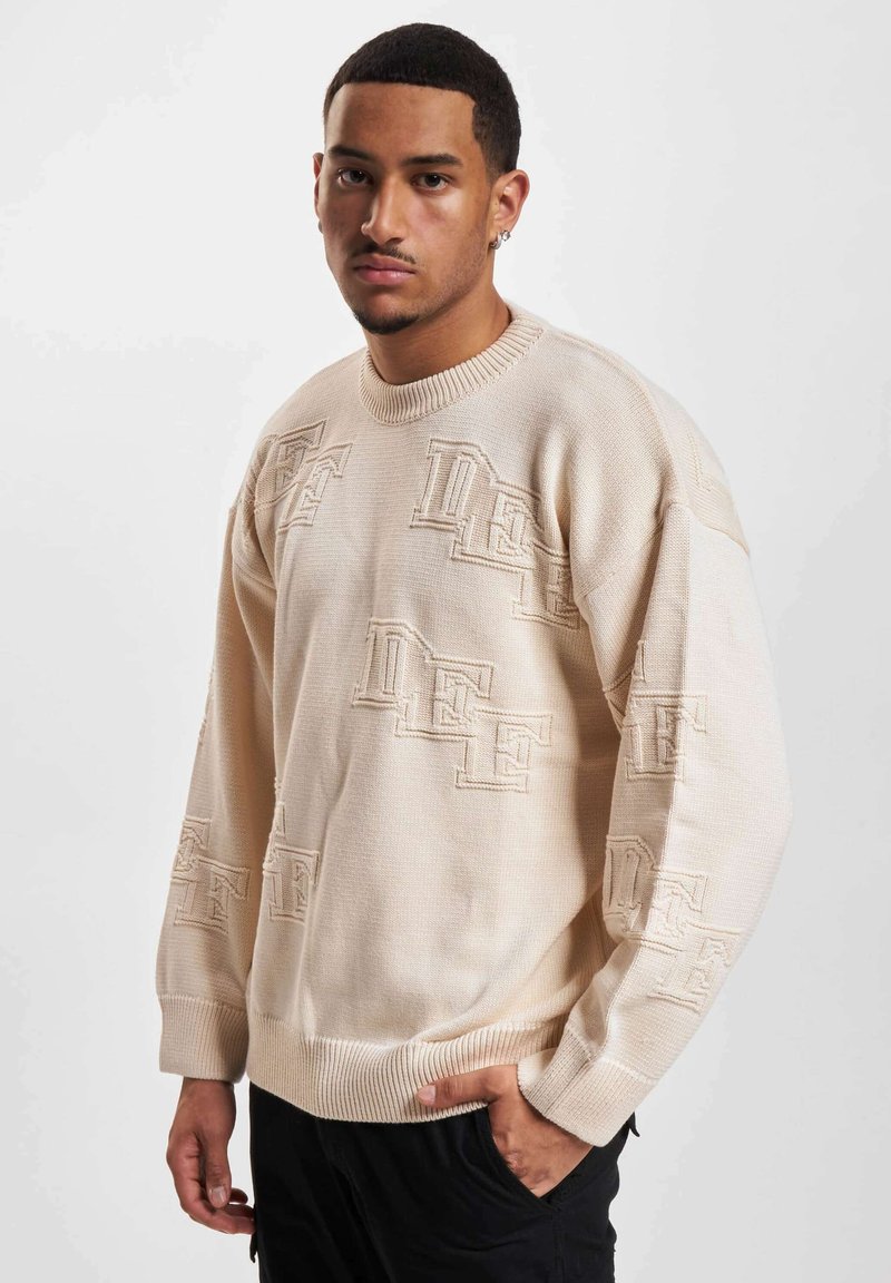 Maglione a maglia beige con motivo logo in rilievo, colletto rotondo e polsini a coste. La vestibilità ampia presenta una superficie testurizzata.