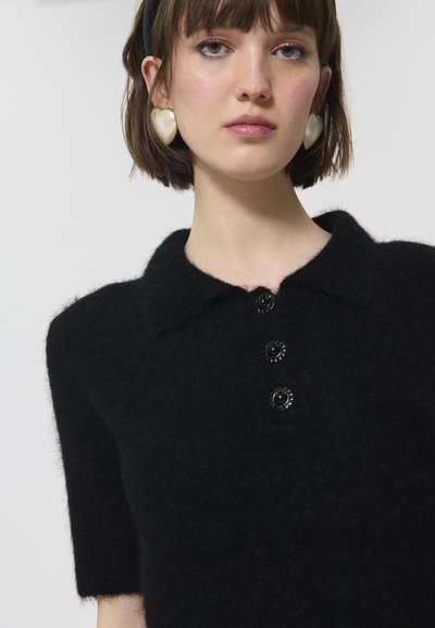 Pulover negru tricotat cu mâneci scurte, guler și trei butoane decorative negre. Textură moale cu un finisaj pufoș.
