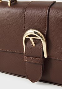 Brown textured handbag with a gold buckle detail. Features a smooth surface and stitched accents, structured design for easy handling.