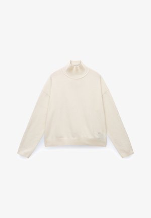 Jersey de cuello alto crema hecho de una tela suave; presenta un cuello y un dobladillo acanalados, hombros caídos y una sutil marca de la marca cerca de la parte inferior.