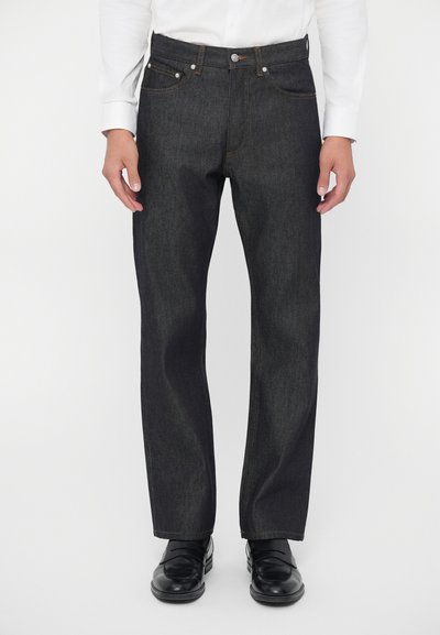 Donkerdenim jeans met een rechte pasvorm, voorzien van oranje stiksels, een knoopsluiting en vijf zakken. Gemaakt met zwarte schoenen.