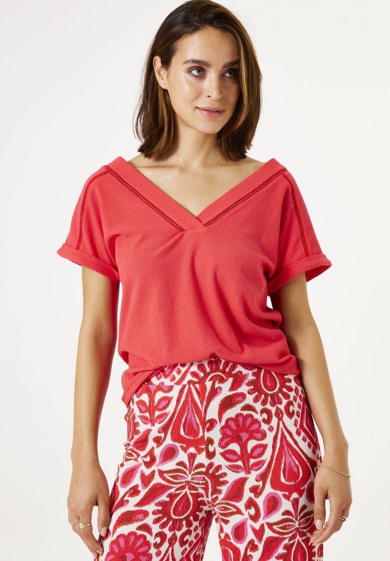 Un haut corail à manches courtes avec un décolleté en V et des coutures décoratives. Assorti à un pantalon fleuri multicolore à motifs.