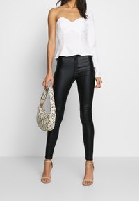 Vit enaxlad topp med hjärtformad halsringning; svarta smala byxor i faux läder; strukturerad väska med ormskinnsmönster; klara remsandaler.