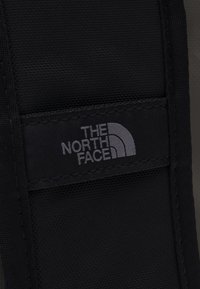 Patch en tissu noir arborant le logo "The North Face" en gris, avec une surface texturée et des bords cousus pour plus de durabilité.