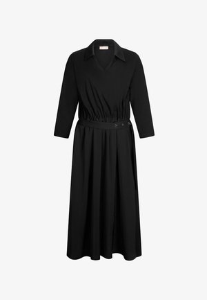 Juoda suknelė su ilgomis rankovėmis ir apykakle. Yra raukšlėta liemens dalis su diržu ir laisvai krintanti sijoninė dalis. Pagaminta iš minkštos medžiagos.