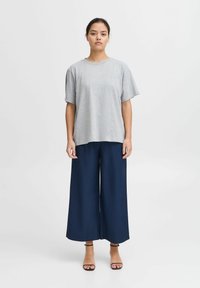 Gray cotton t-shirt with short sleeves paired with wide-legged navy trousers. Model wears black strappy sandals, standing against a plain background.