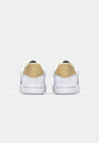 Valged sneakersid, mille ülemine osa on siledast nahast, kuldsete detailidega kontsapooles ja reljeefne logo tallal. Ümar varvas ja klassikaline lipsukujundus.
