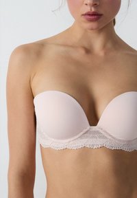 Różowa biustonosz bez ramiączek z gładkimi, wyściełanymi miseczkami i koronkowym wykończeniem u dołu, z falistymi krawędziami i misternymi detalami.