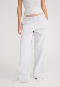 Pantaloni della tuta grigi chiari con una vestibilità comoda, vita elastica e tasche. Il materiale sembra morbido con una texture liscia.