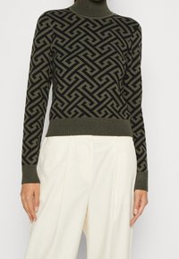 Turtleneck-Pullover in Olivgrün mit einem geometrischen schwarzen Muster. Gerippte Bündchen und Saum, aus einem weichen Strickmaterial gefertigt.