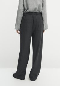 Zwarte wijde broek met een streeppatroon, gemaakt van een zachte stof. Voorzien van een elastische tailleband en twee achterzakken.