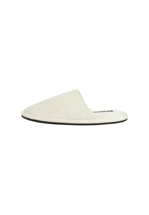 Pantofole bianche in tessuto con motivo trapuntato, punta aperta e suola nera, caratterizzate da una parte superiore curva e una texture morbida.
