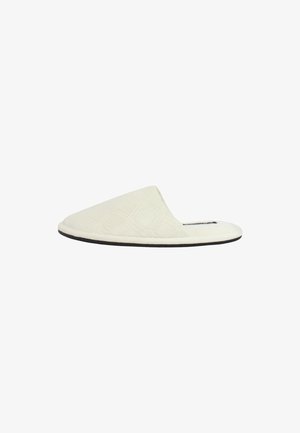 Pantofole bianche in tessuto con motivo trapuntato, punta aperta e suola nera, caratterizzate da una parte superiore curva e una texture morbida.