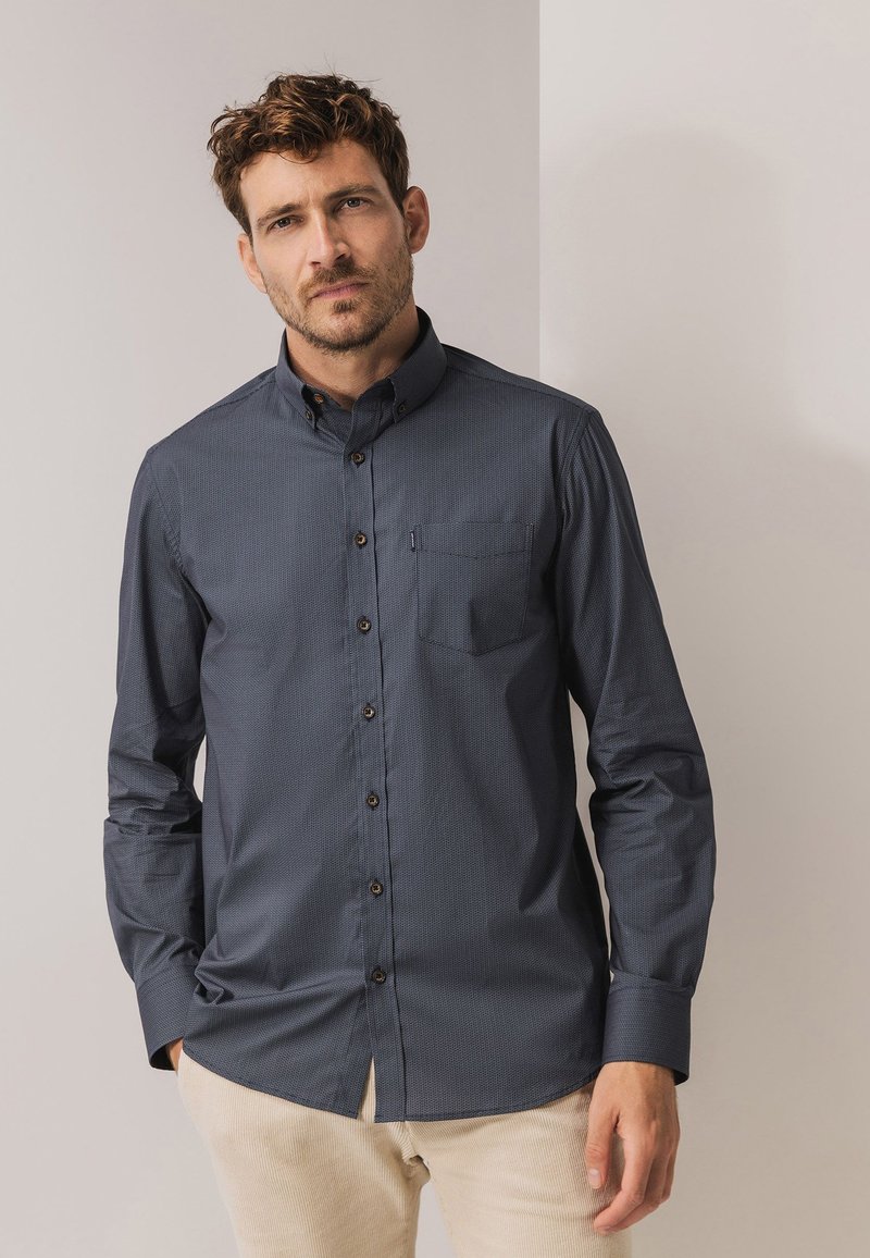 Navy button-down shirt with a subtle pattern, featuring a pocket, brown buttons, and long sleeves, made from a smooth fabric.