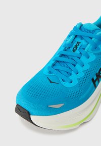 Μπλε αθλητικό παπούτσι με επάνω μέρος από δίχτυ, υφή σχεδίου και μαύρη σόλα. Διαθέτει έντονα κορδόνια, λεπτομέρεια λογότυπου και πράσινη απόχρωση στη σόλα.