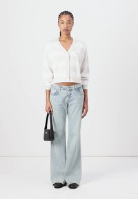 Cárdigan de rayas gris claro, diseño corto con botones; combinado con jeans de pierna ancha en azul claro; sosteniendo un pequeño bolso negro.