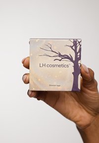 Cosmetica productdoos met een boomontwerp in paars, met een schitterende achtergrond. De tekst luidt "LH cosmetics" en "Shimmer saga."