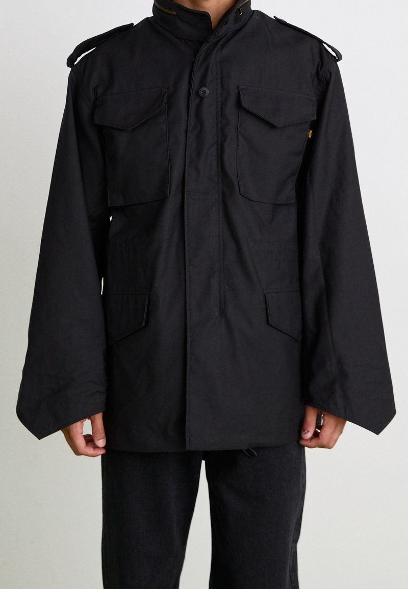 Czarna kurtka wierzchnia z długimi rękawami, dwoma przednimi kieszeniami z klapami, zapięciem na guziki oraz naramiennikami. Wykonana z teksturowanej tkaniny.