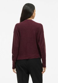 Pull en tricot bordeaux avec texture côtelée, épaules tombantes et design court. Il est doté de manches longues et d'un ourlet droit.