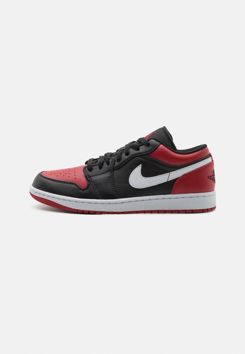 Baskets basses noires, rouges et blanches avec un swoosh Nike blanc et une semelle extérieure rouge, visibles de côté gauche sur un fond uni.