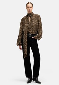 Blusa de estampado de leopardo en marrón y negro con cuello alto y mangas largas, combinada con pantalones de terciopelo negro y botines de punta.