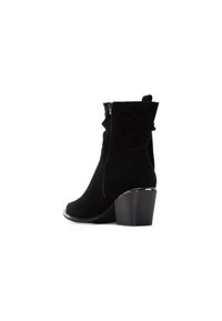 Botines de ante negros con punta ligeramente afilada, cremallera lateral y tacón afilado. Presentan una textura suave y un diseño minimalista elegante.