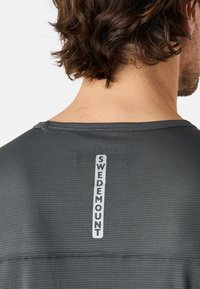 Grå prestations-t-shirt med ett strukturerat mönster, rundad halsringning och en vertikal "SWEDEMOUNT"-logotyp på baksidan. Ljusreflekterande detaljer.