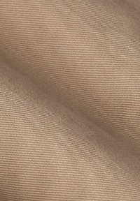 Beige stof met een soepele textuur en een fijne ribbelpatroon, die zachte drapering en een subtiele glans laat zien in natuurlijk licht.