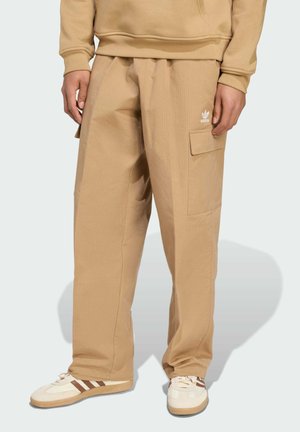 Beige cargo bukser i tekstureret stof med en sidelomme og Adidas-logoet i hvid. Sæt sammen med hvide og brune sko.