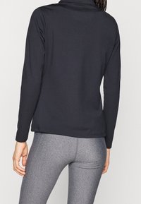 Svart långärmad topp med en figurnära design, slät textur och hög krage. Matchas med grå leggings med ett subtilt melerat mönster.