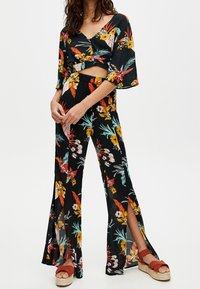 To-delt outfit i let sort stof med livlige blomster mønstre. Toppen har klokkeærmer, og bukserne har sideslids.