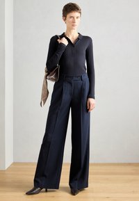 Top de manga longa ajustado, em ribana escura com colarinho, combinado com calças largas de risca de giz azul marinho de cintura alta e sapatos de salto agudo escuros.