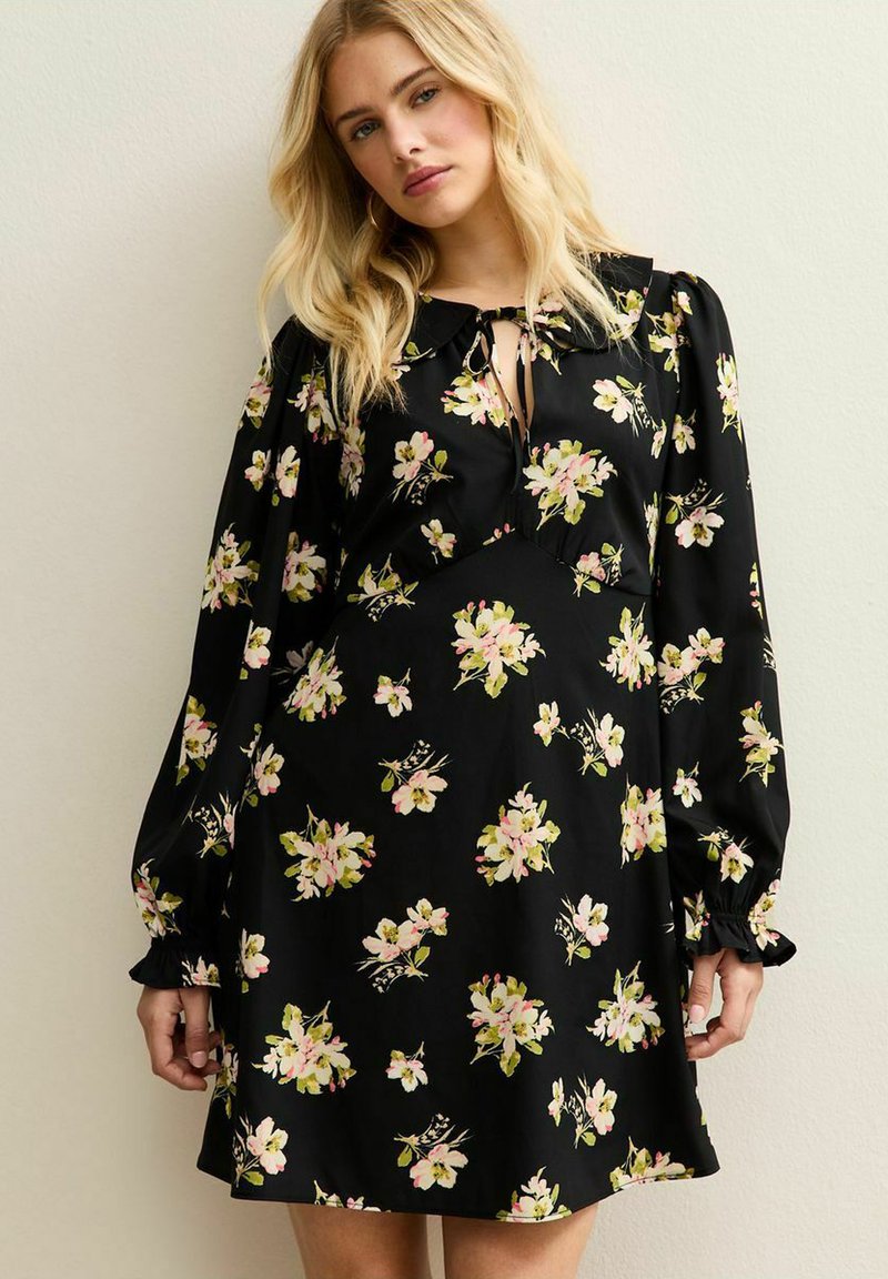 Robe noire avec de longues manches bouffantes, motif floral de fleurs roses et vertes, décolleté en forme de trou et poignets froncés. Texture de tissu douce.